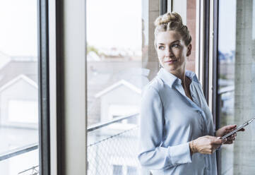 Smiling businesswoman standing with tablet PC in office - UUF30392