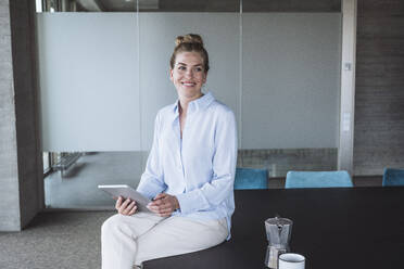 Happy businesswoman sitting on desk with tablet PC - UUF30398