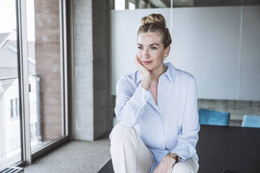 Thoughtful businesswoman sitting with hand on chin in office - UUF30400