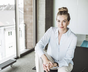 Smiling businesswoman sitting with hands clasped on desk - UUF30403