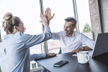 Happy businessman giving high-five to businesswoman in office - UUF30423