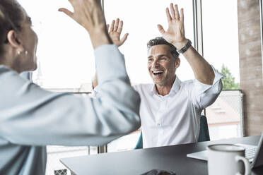 Happy businessman giving high-five to colleague at desk - UUF30426
