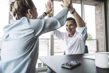 Smiling mature businessman giving high-five to colleague at desk in office - UUF30429
