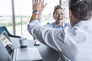 Happy businesswoman giving high-five to colleague at desk in office - UUF30430