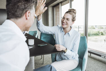 Happy businesswoman giving high-five to colleague in office - UUF30431