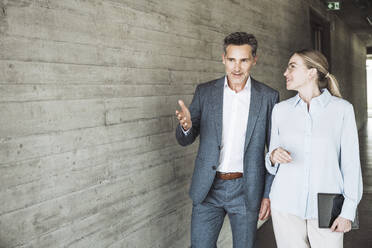 Businessman gesturing and discussing with businesswoman near wall - UUF30442