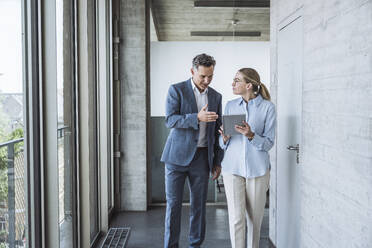 Mature businessman discussing with colleague over tablet PC - UUF30446