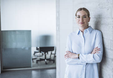 Smiling businesswoman standing near wall in office - UUF30459