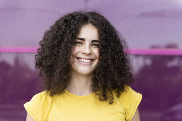 Smiling curly haired woman in front of pink wall - LMCF00565