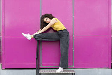 Smiling woman stretching leg in front of pink wall - LMCF00568