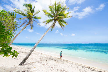 Mann in Badekleidung und Tropenhemd an einem schönen tropischen Sandstrand - Tropischer Strand mit blauem Wasser und Palmen - DMDF04901