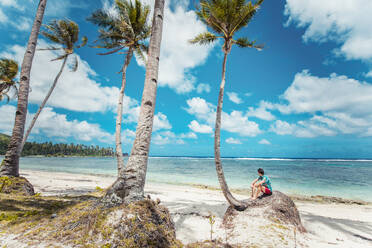 Man wearing swimwear and tropical shirt on a beautiful sandy tropical beach - Tropical beach with blue water and palm trees - DMDF04905