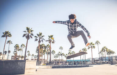 Cool skateboarder outdoors - Afroamerican guy jumping with his skate and performing a trick - DMDF04997