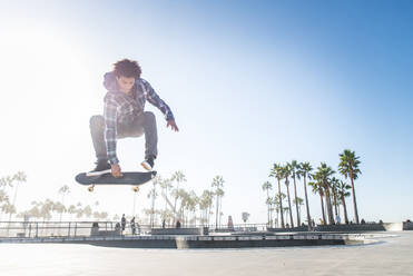 Cool skateboarder outdoors - Afroamerican guy jumping with his skate and performing a trick - DMDF04999