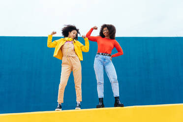 Young happy women posing on colored blue and yellow colored walls. Teenagers girl spending time together after school - DMDF05161