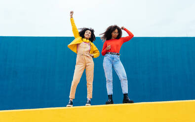 Young happy women posing on colored blue and yellow colored walls. Teenagers girl spending time together after school - DMDF05162