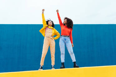 Young happy women posing on colored blue and yellow colored walls. Teenagers girl spending time together after school - DMDF05164