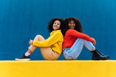 Young happy women posing on colored blue and yellow colored walls. Teenagers girl spending time together after school - DMDF05166