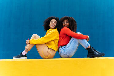 Young happy women posing on colored blue and yellow colored walls. Teenagers girl spending time together after school - DMDF05167