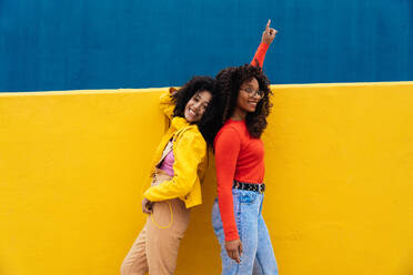 Young happy women dancing and having fun outdoor. Teenagers listening to music with smartphone and headphones in a yellow and blue modern urban area - DMDF05172