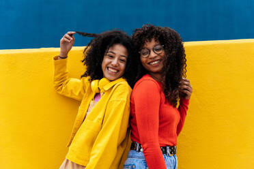 Junge glückliche Frauen tanzen und haben Spaß im Freien. Teenager hören Musik mit Smartphone und Kopfhörern in einem gelben und blauen modernen Stadtgebiet - DMDF05173