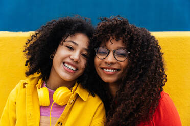 Junge glückliche Frauen tanzen und haben Spaß im Freien. Teenager hören Musik mit Smartphone und Kopfhörern in einem gelben und blauen modernen Stadtgebiet - DMDF05176