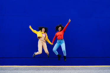 Young happy women dancing and having fun outdoor. Teenagers listening to music with smartphone and headphones in a yellow and blue modern urban area - DMDF05190