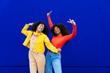 Young happy women dancing and having fun outdoor. Teenagers listening to music with smartphone and headphones in a yellow and blue modern urban area - DMDF05191