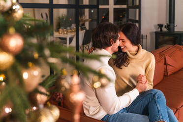 Happy beautiful couple of lovers celebrating Christmas at home - Winter holiday season, celebration of xmas eve in a decorated apartment - DMDF05370