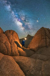 Silhouette of unrecognizable traveler with flashlight standing on top of stone mountain formation admiring majestic night starry milky way sky in Vermilion Cliffs, National Monument in Arizona , USA - ADSF47194