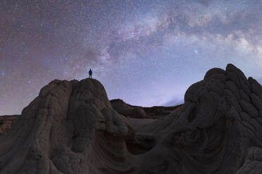 Von unten Silhouette von unerkennbaren Touristen, die auf dem Gipfel einer steinernen Bergformation stehen und den majestätischen nächtlichen Sternenhimmel in Vermilion Cliffs, National Monument in Arizona, USA, bewundern - ADSF47197