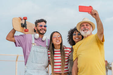Happy diverse friends wearing trendy outfits standing and taking selfie on smartphone while enjoying and having fun together - ADSF47222