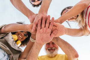 Low angle of cheerful friends in casual clothes stacking hands outside and looking down while having fun together - ADSF47223