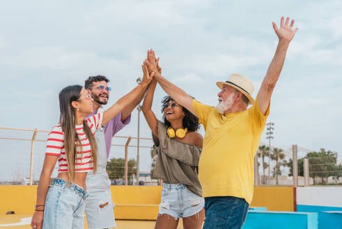 Happy multiethnic family unit with raised arms and enjoying vacation while having fun together against blurred background of playground in city - ADSF47224