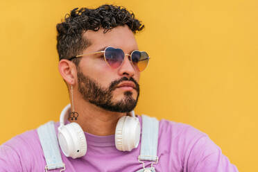 Portrait bearded male with headset and eyewear looking away thoughtfully against yellow background in studio shot - ADSF47230