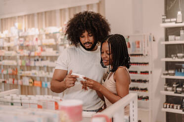 Junger schwarzer Freund mit Afro-Haar und Freundin mit Dreadlocks halten und lesen Informationen aus Medizin-Paket und Lesen von Informationen beim Kauf von Apotheke speichern - ADSF47245