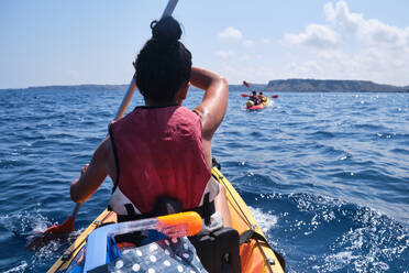 Back view of unrecognizable female traveler rowing kayak with paddle while floating on rippling sea during summer trip in tropical resort - ADSF47288