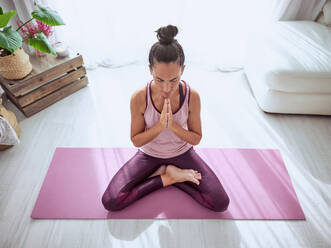 From above full body of peaceful female in sportswear meditating in Padmasana pose with namaste hands during yoga practice on mat - ADSF47292