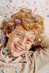 Happy blond kid smiling and looking at camera in confetti with hands on head - ADSF47314