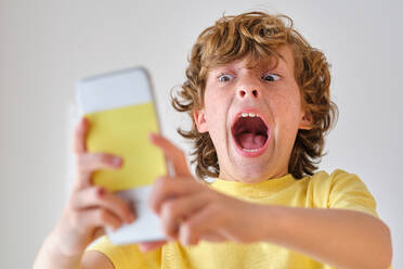 Frightened child with open mouth shouting while taking self portrait on cellphone in daytime - ADSF47321