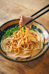 High angle of ornamental bowl of delicious Japanese noodle soup under soft meat piece between food sticks - ADSF47361