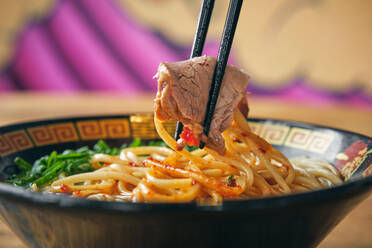 Ornamental bowl of traditional Japanese noodle soup with salsa and soft meat piece between food sticks - ADSF47363