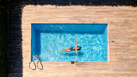 Drone view full body of anonymous lady with long wet dark hair chilling in water of outdoor swimming pool and sunbathing on summer day in yard - ADSF47380