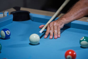 Unrecognizable male leaning on pool table and preparing to strike ball with cue while playing snooker at home - ADSF47418