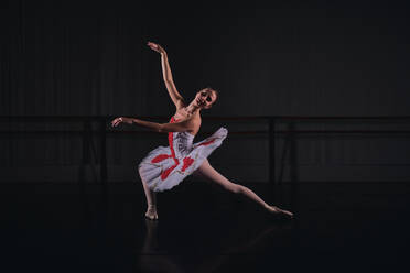 Full body of sensual ballerina in scenic costume and tutu dancing ballet role while rehearsing in dark studio - ADSF47422