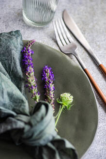 High angle of autumnal table setting with marbled plate, napkin, fork and knife and lavender flowers against gray surface - ADSF47484