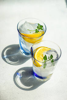 High angle of Summer cocktails with lemon vodka, slices of lemon and wild mint leaves served with ice placed on white table - ADSF47487