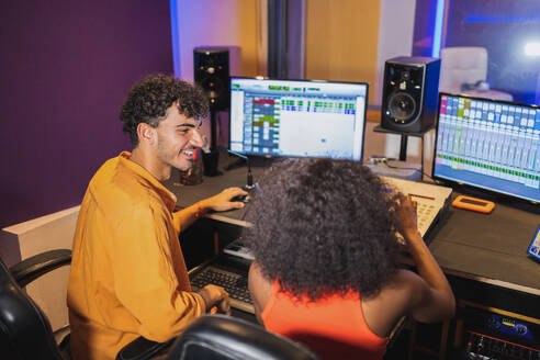 Male audio engineer and female African American vocalist enjoying recorded song in control room with computer sound software and mixing board - ADSF47499