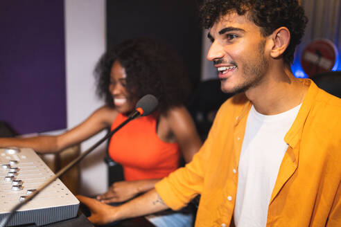 Male audio engineer and optimistic female African American singer creating hit song while using mixing board and computer software in musical studio - ADSF47500