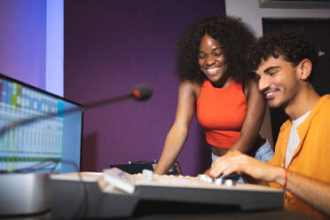 Male audio engineer and optimistic female African American singer creating hit song while using mixing board and computer software in musical studio - ADSF47504